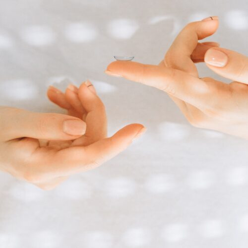 Two hands up close holding contact lenses on the pointer finger of each hand