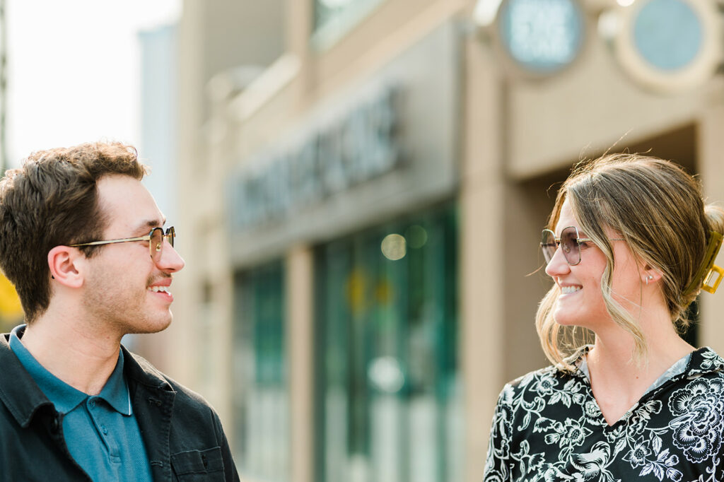 a man and woman stand facing one another outside a Kamloops eye clinic to test their transition lenses outdoors