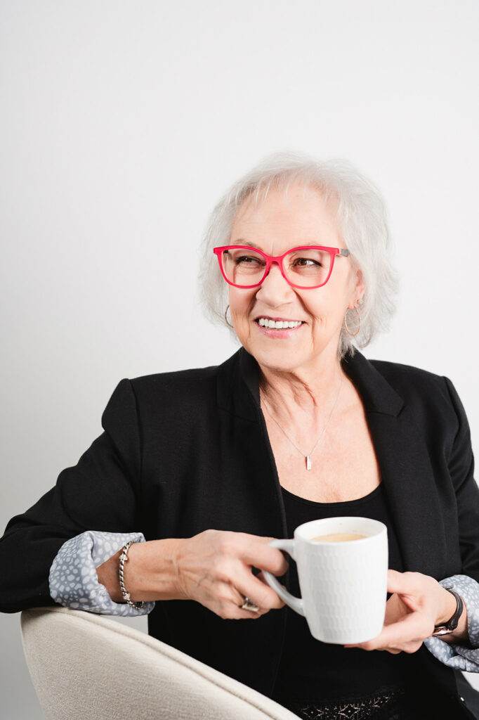 woman in blazer wearing red glasses enjoys a coffee and smiles in kamloops bc optometrists office
