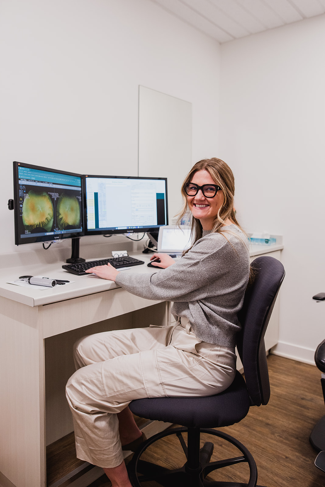Woman working at a desk inside an optometry clinic, focused on a computer screen.