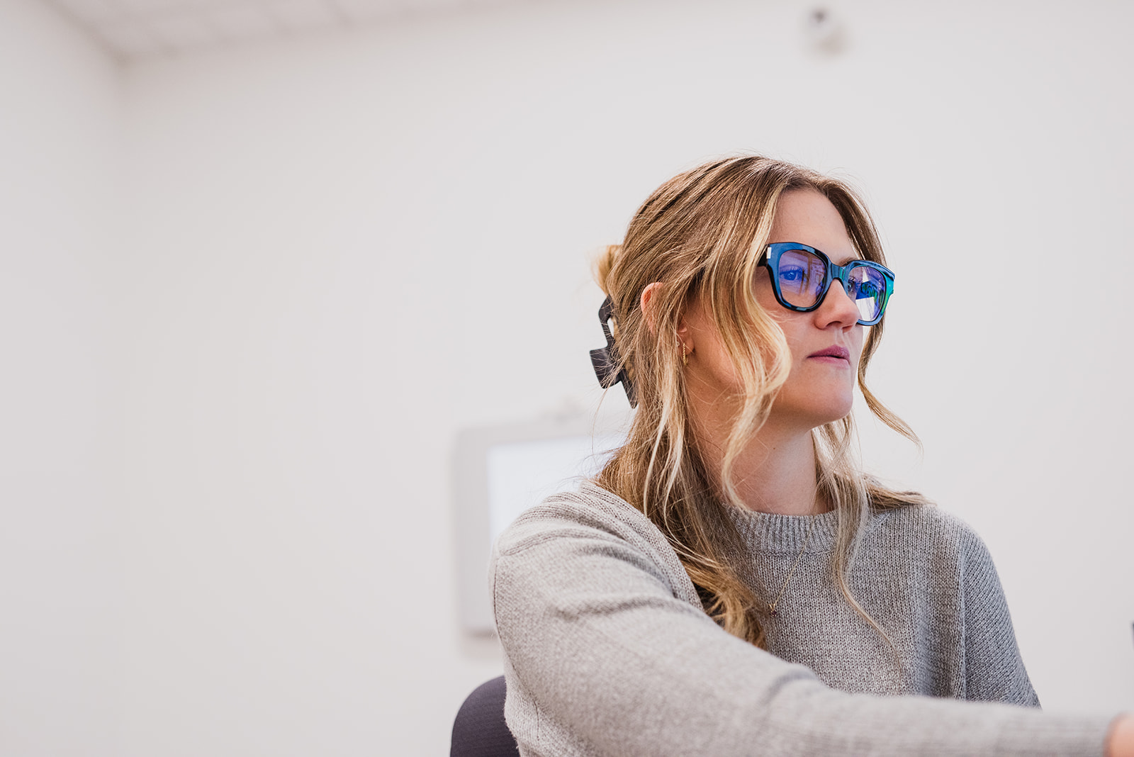 Woman wearing blue-light glasses while working at a desk inside an optometry clinic, focused on a computer screen.
