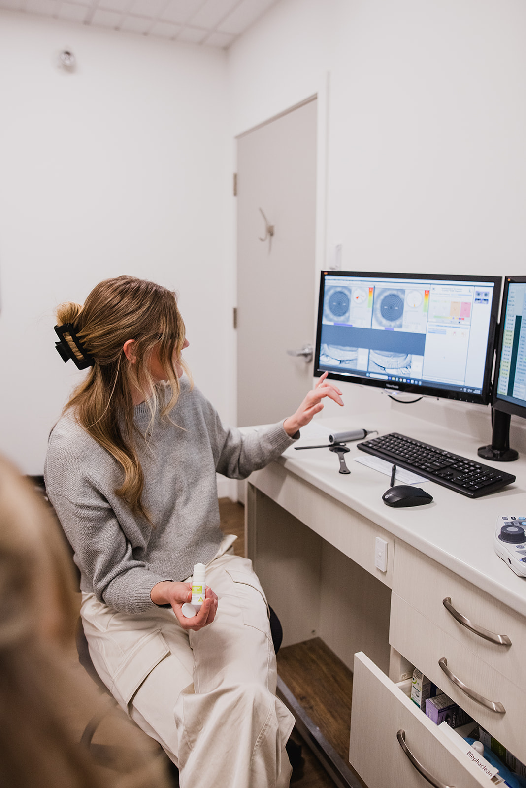 Woman working at a desk inside an optometry clinic, focused on a computer screen.